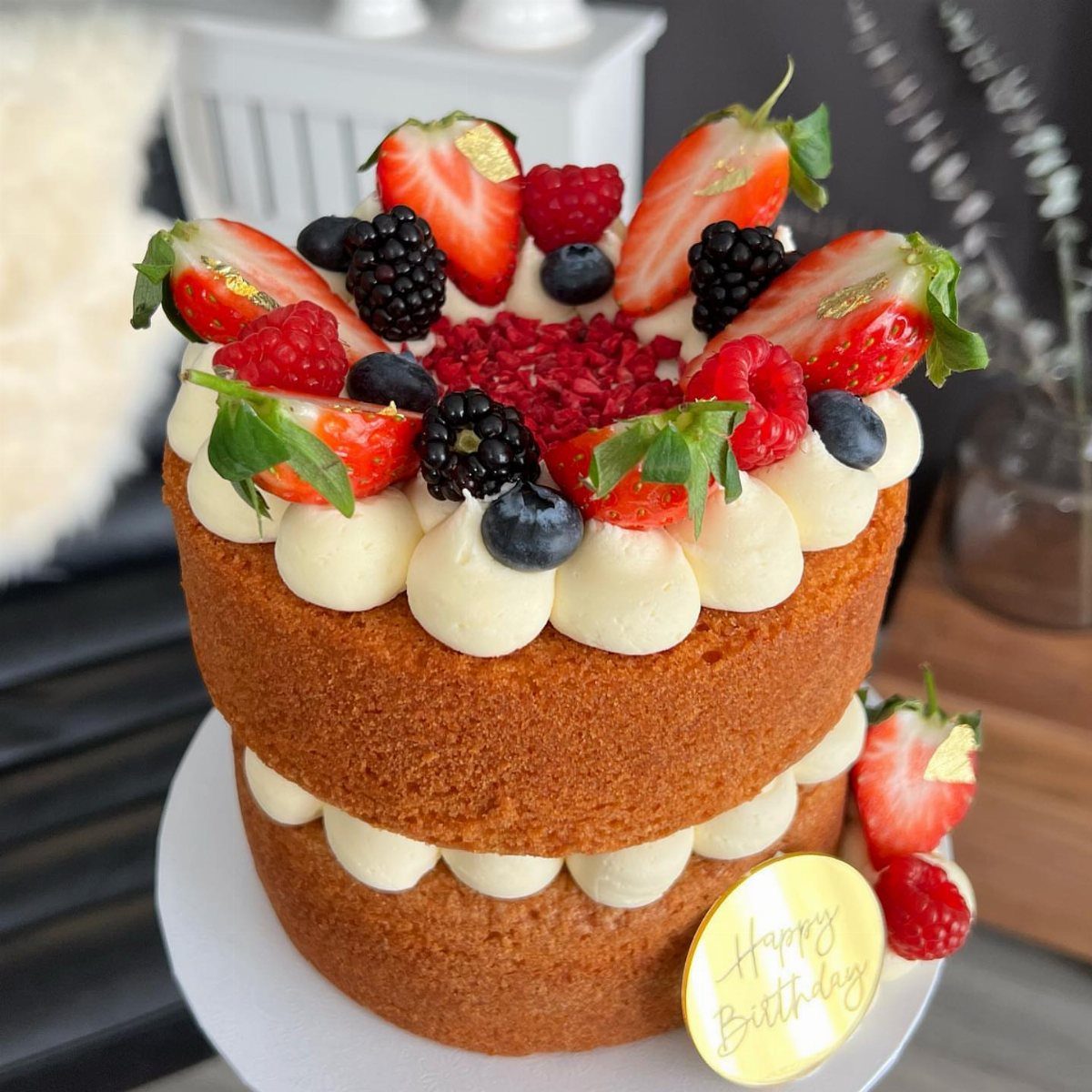 Two-layer sponge cake topped with fresh berries and cream with a birthday sign.