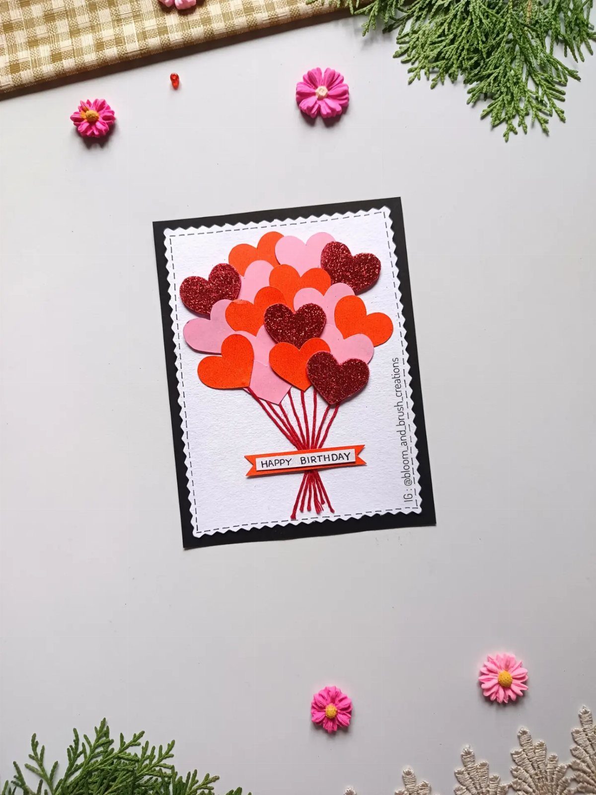 Handmade birthday card with heart-shaped balloons in red and pink on white paper.