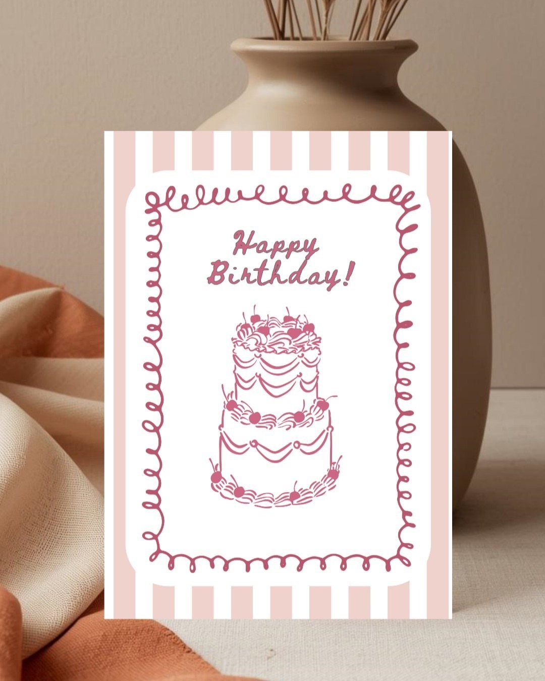 Birthday card with pink stripes and a cake illustration leaning against a vase.