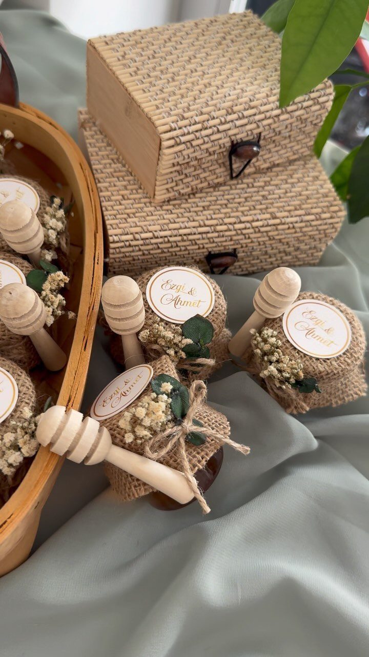 Small honey jars with burlap lids and flowers as wedding favors on green fabric