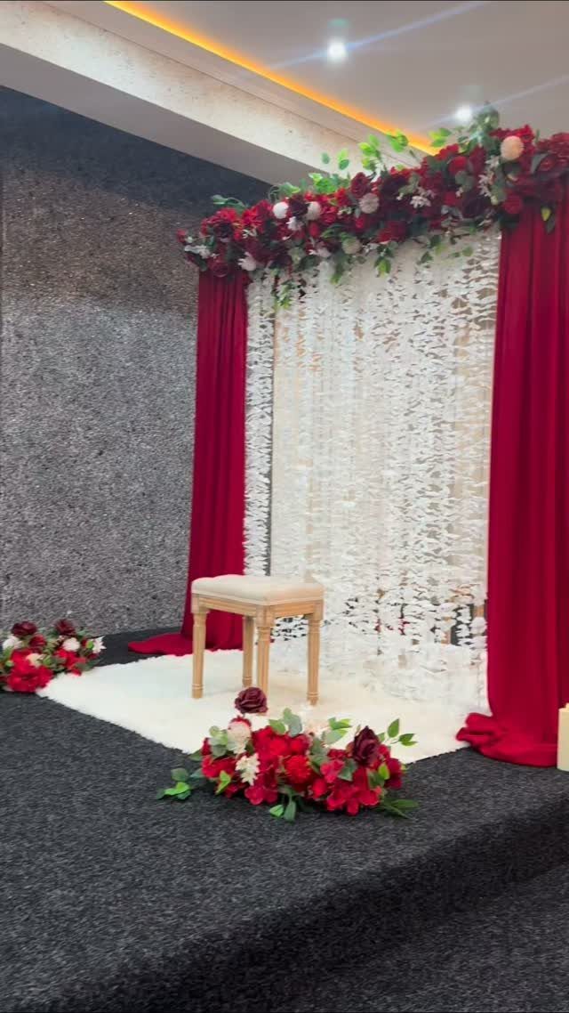 Wedding backdrop with red curtains, white floral wall, and red flower arrangements.