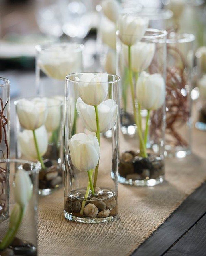 White tulips in glass cylinder vases with river stones on a burlap runner