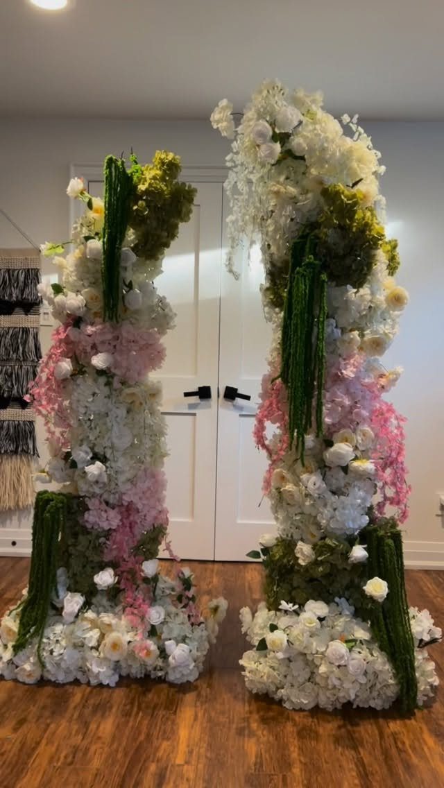 Two tall floral pillars with white and pink flowers and green foliage indoors.