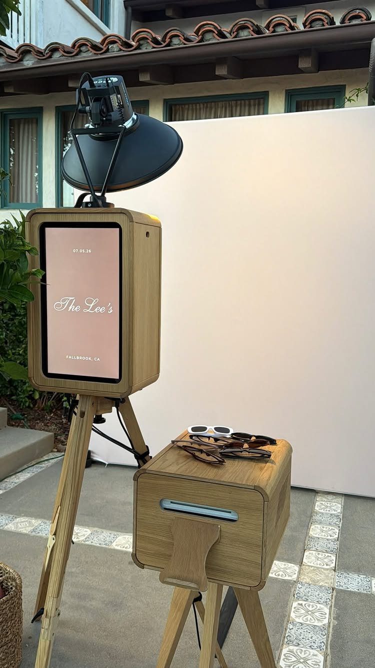 Wooden photo booth with digital screen and white backdrop on a tiled patio