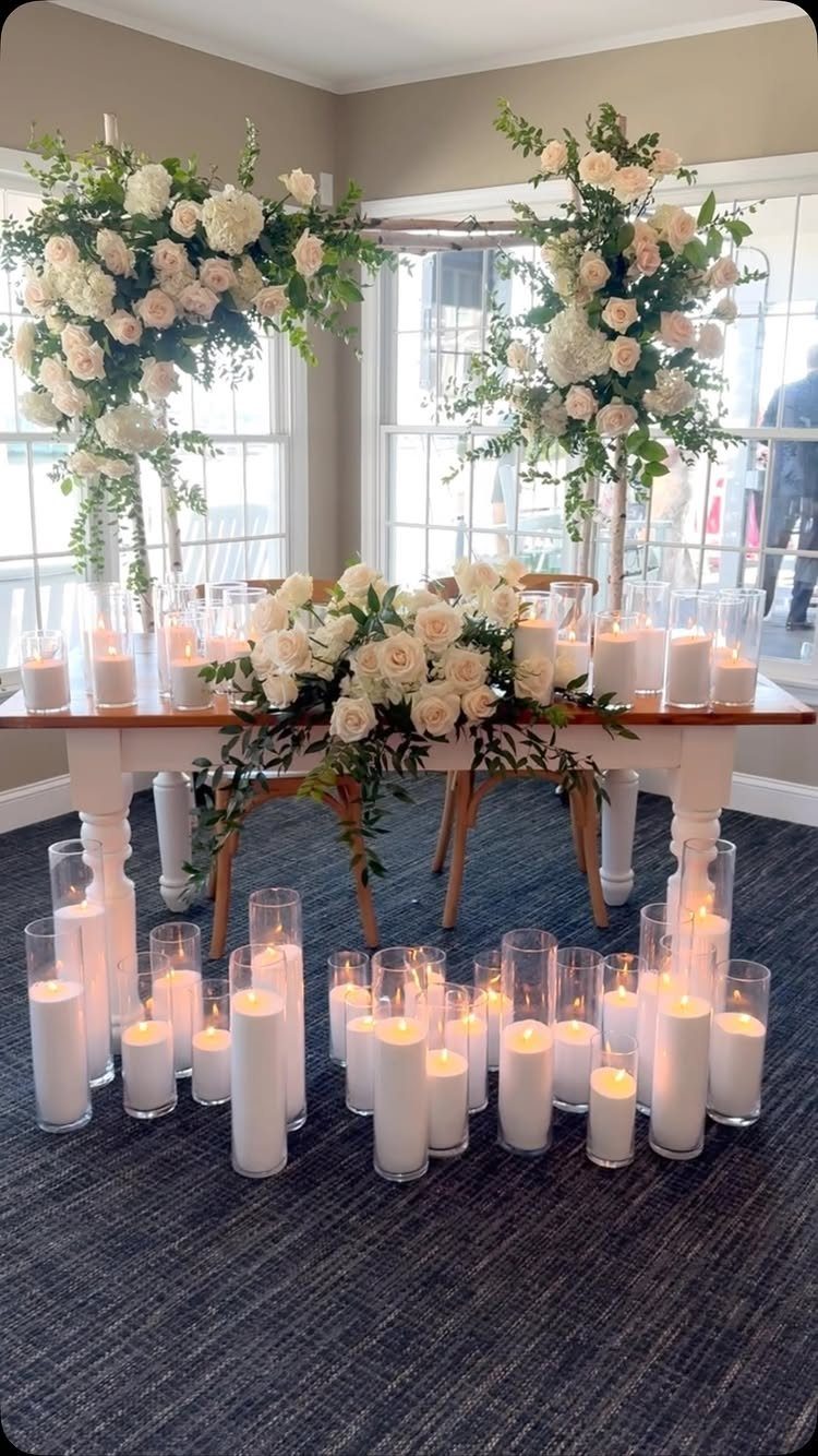 White wooden sweetheart table decorated with white roses and many glowing pillar candles.