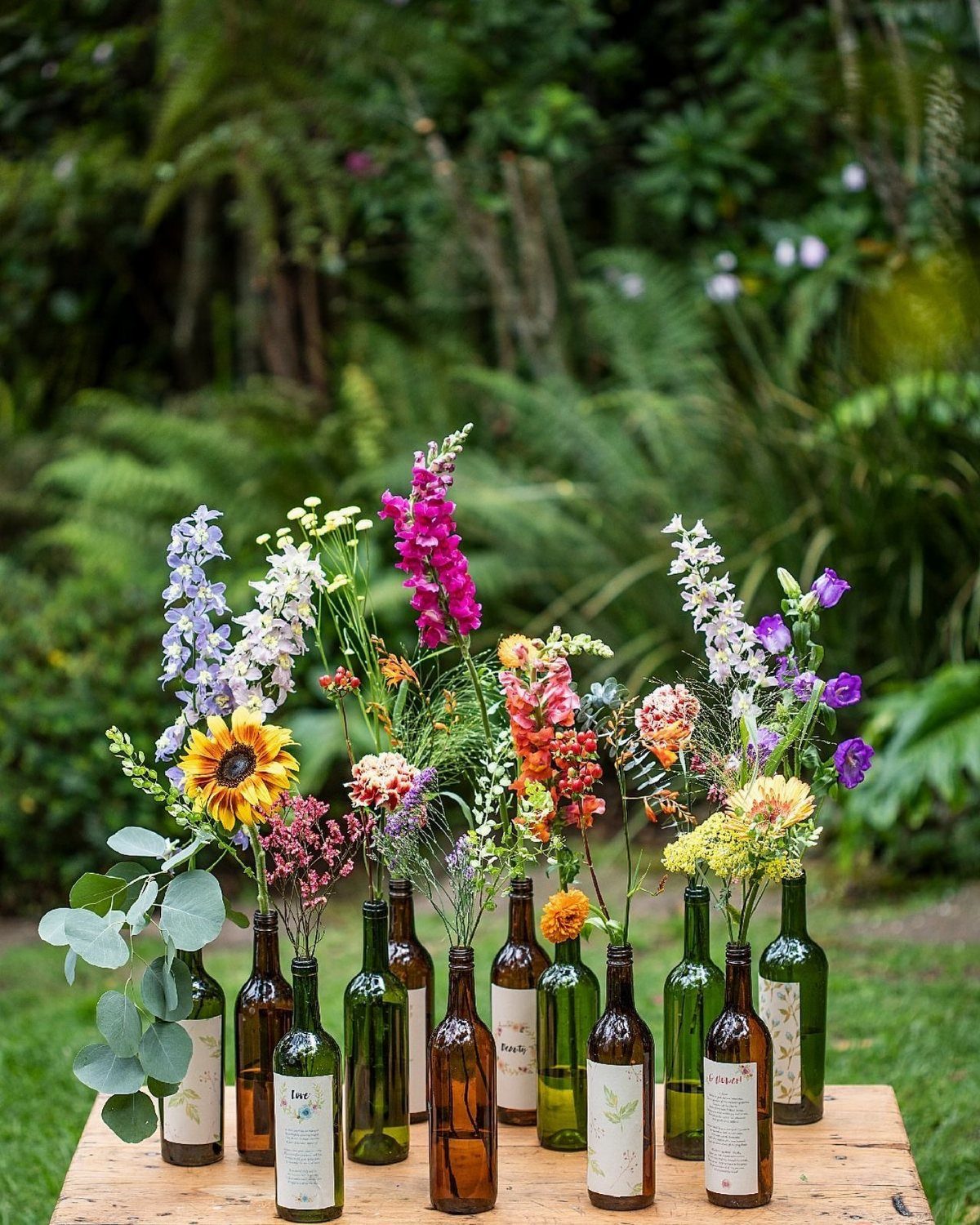 Wine bottles used as vases for colorful wildflowers on a wooden outdoor table.