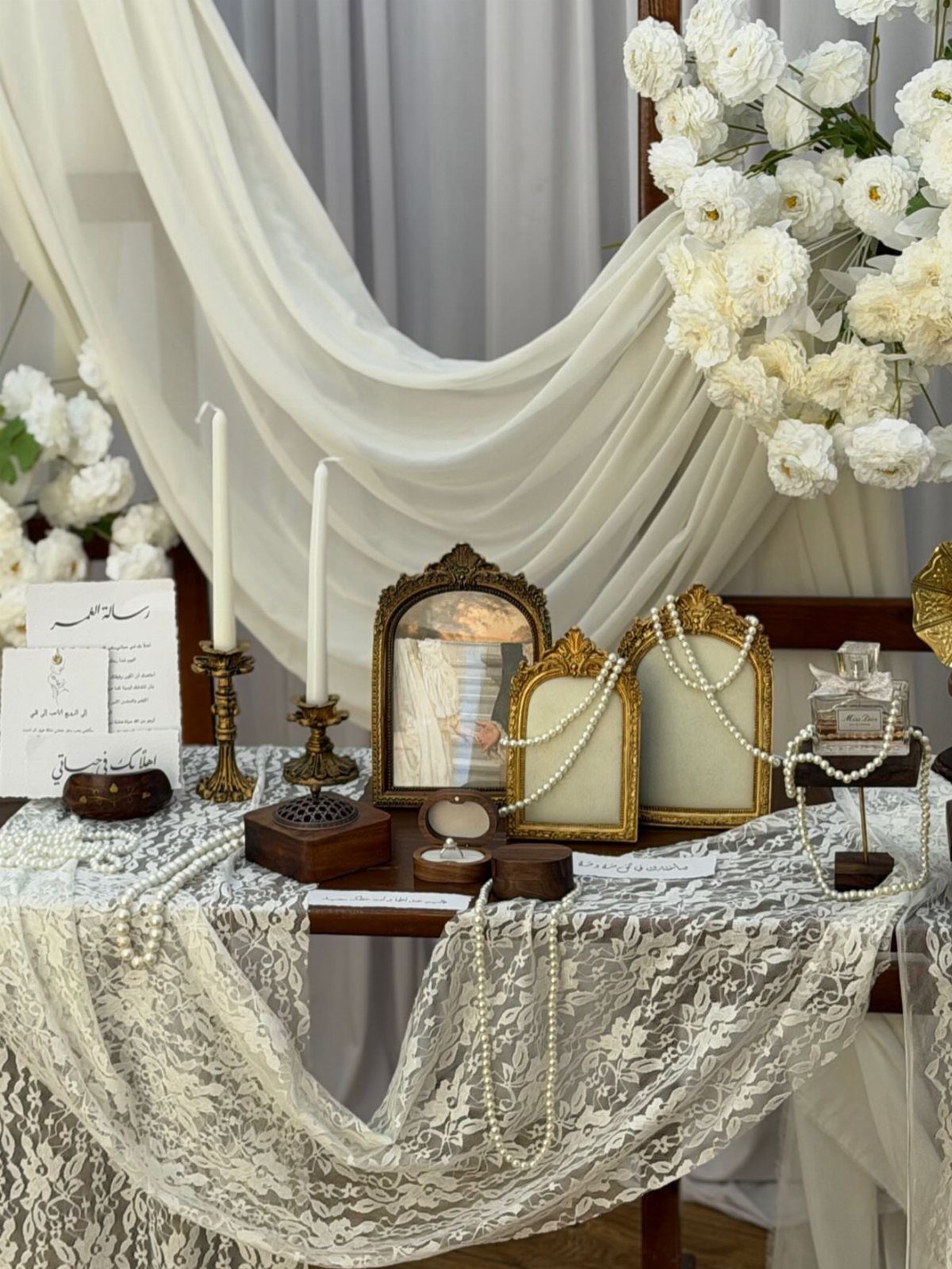 Decorated wedding table with lace cloth, gold mirrors, white candles, and pearls.