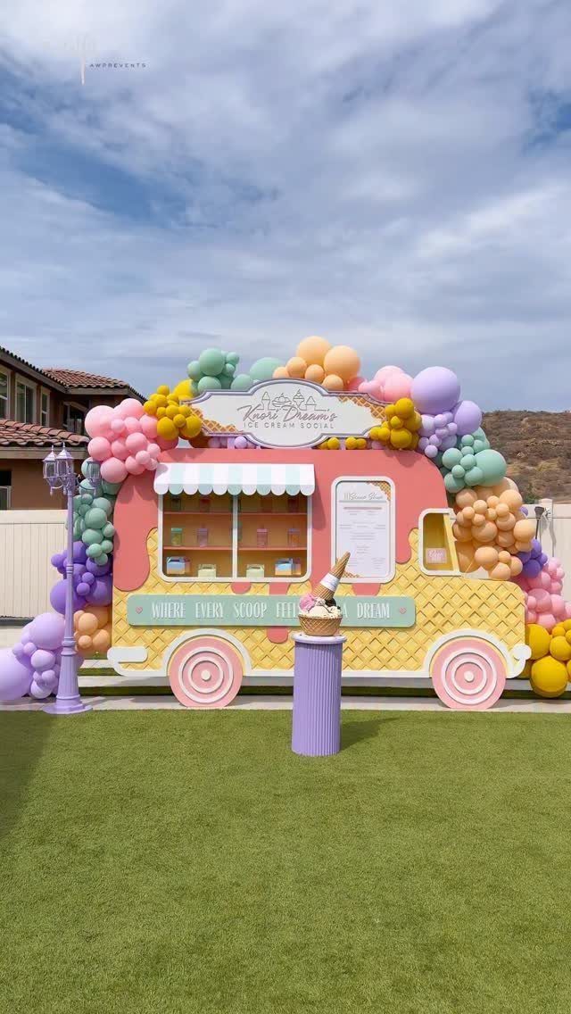 Ice cream truck cutout decorated with pastel balloons on a green lawn.