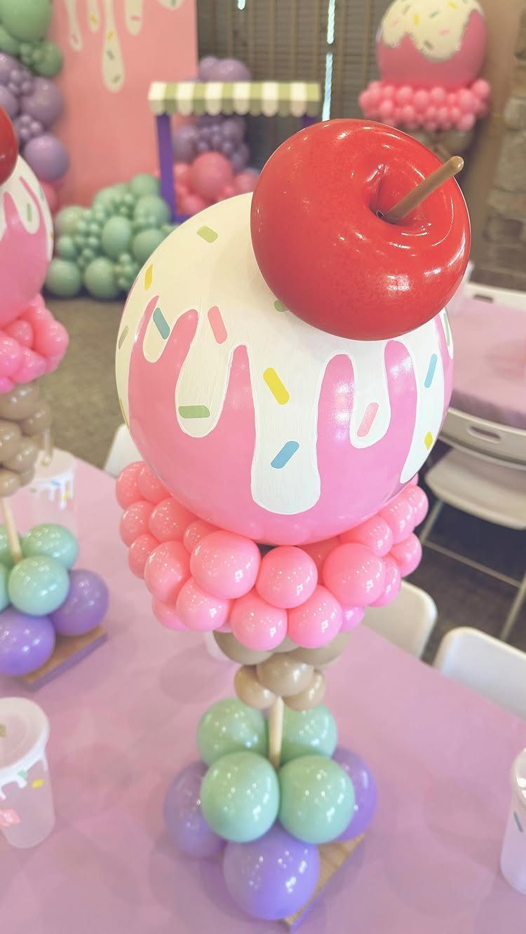 Ice cream sundae balloon sculpture with pink icing and a red cherry topper.