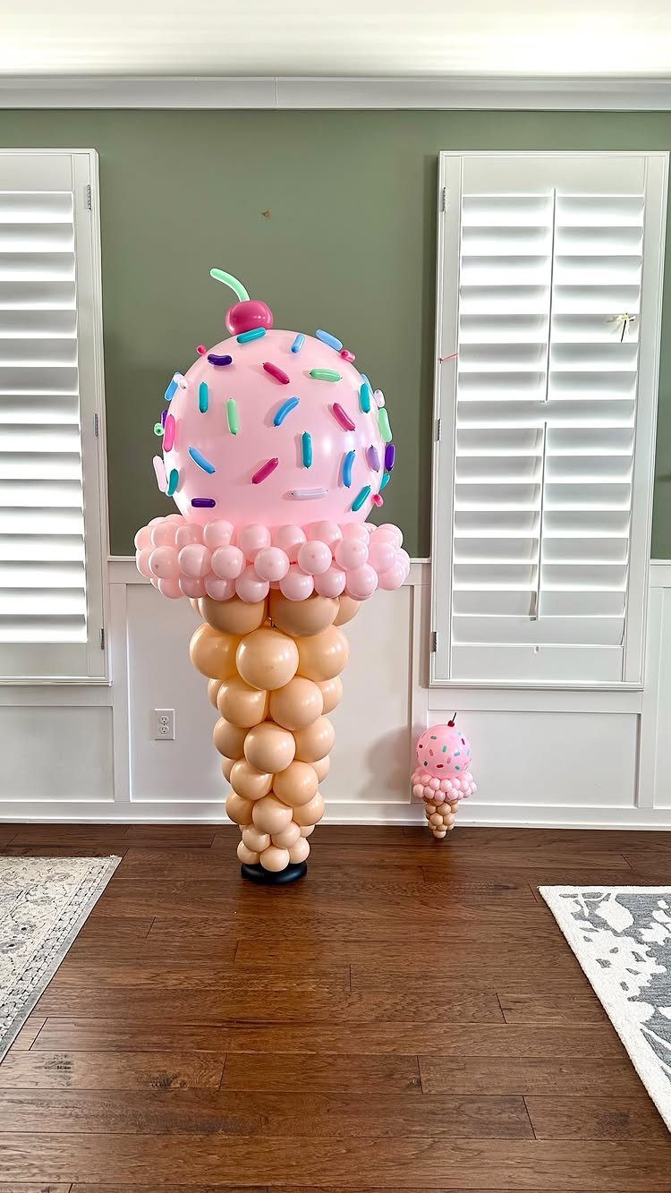Large ice cream cone balloon sculpture with pink scoops and colorful sprinkles.