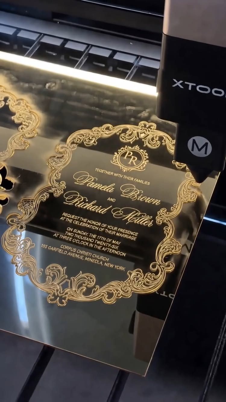 Laser engraving machine cutting an ornate gold acrylic wedding invitation with elegant text.