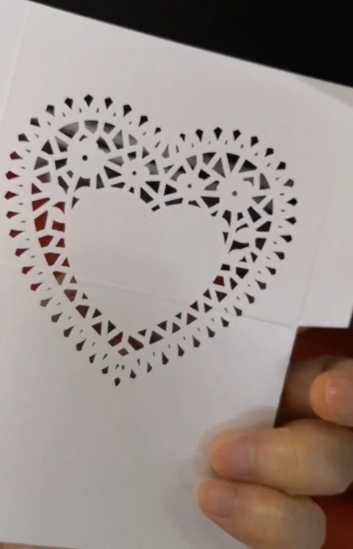 White laser-cut wedding invitation with an intricate heart pattern held by a hand.