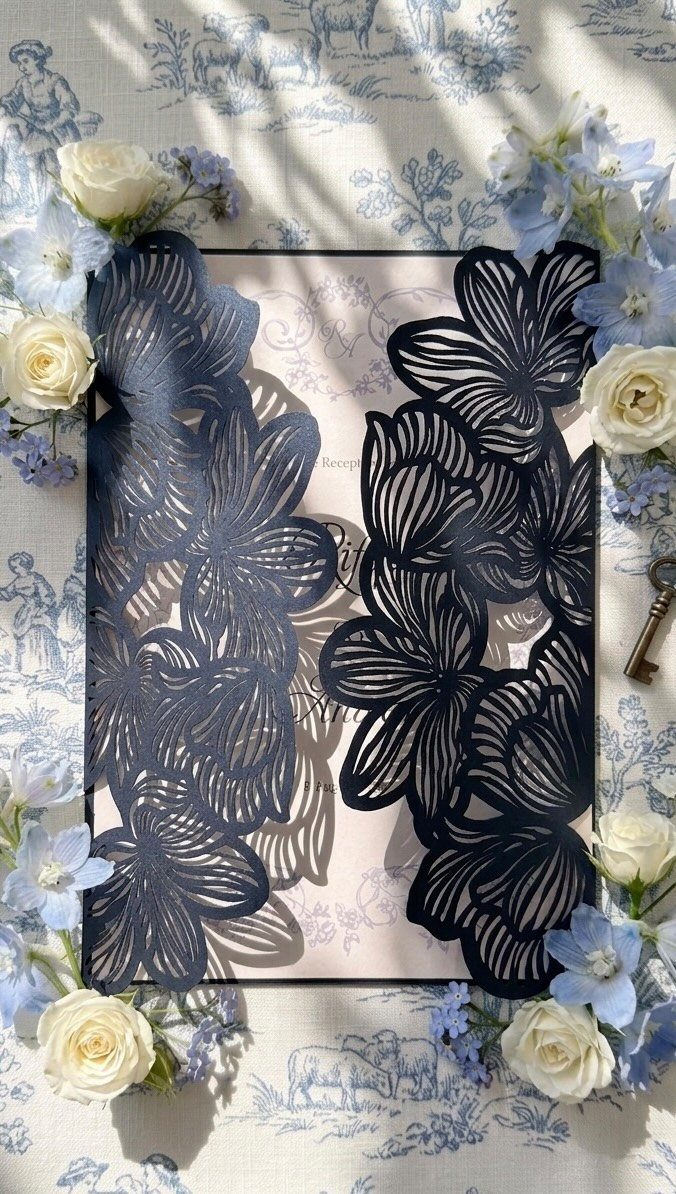Dark blue laser-cut floral wedding invitation sleeve surrounded by white and blue roses.