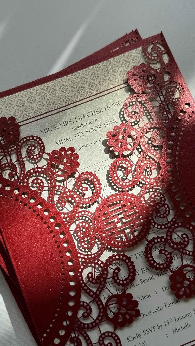 Red laser-cut wedding invitation with intricate patterns over a white printed card.