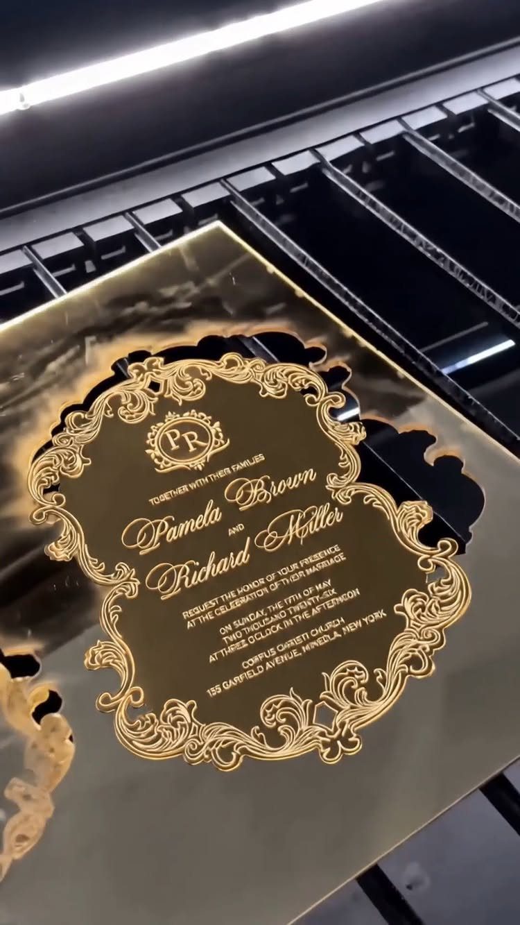 Gold laser-cut wedding invitation with ornate borders resting on a machine grid.