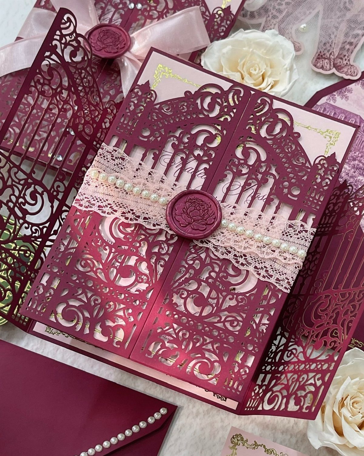 Burgundy laser-cut wedding invitations adorned with a lace ribbon and wax seal.