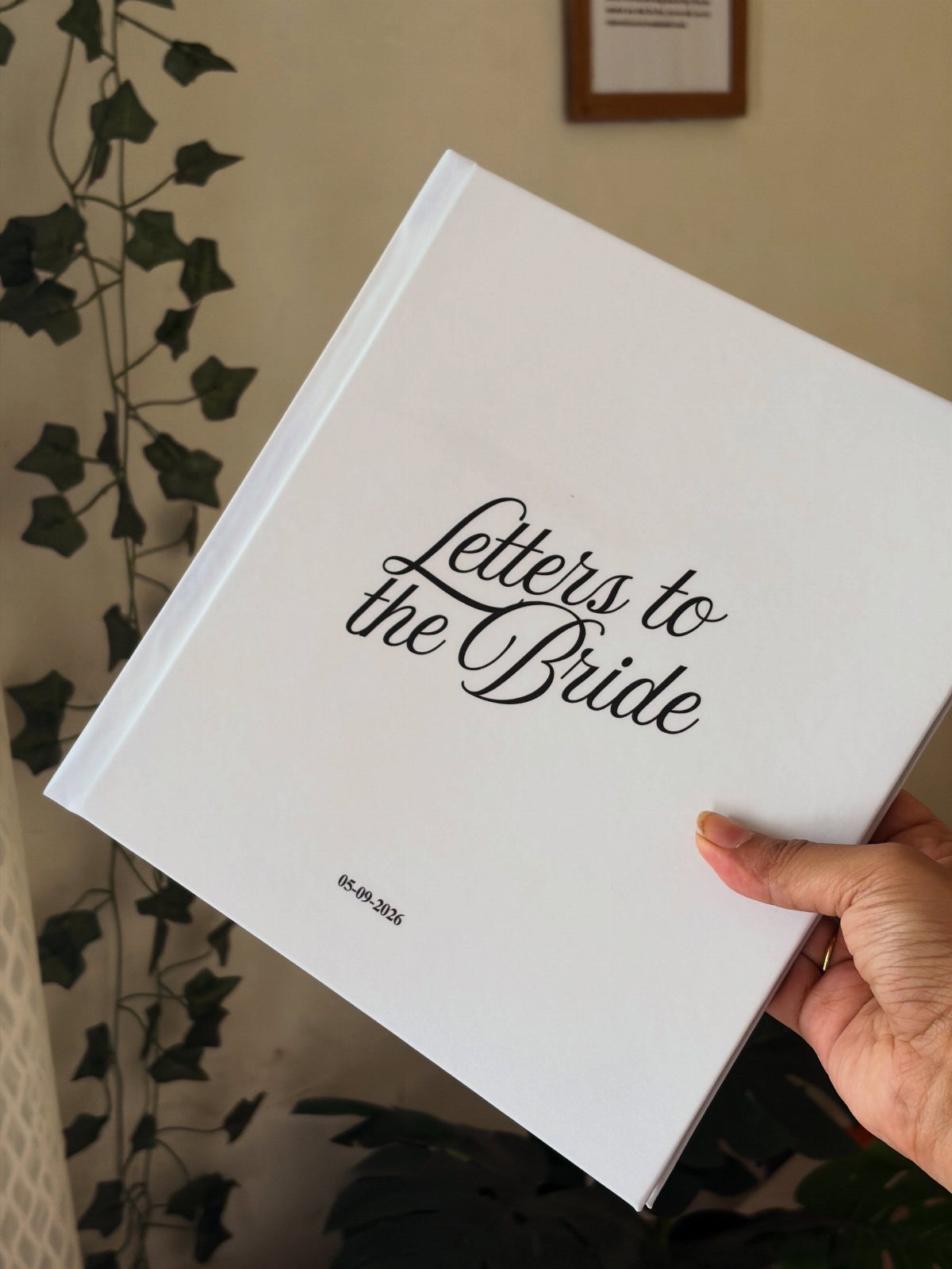 White hardcover scrapbook titled Letters to the Bride held by a hand.