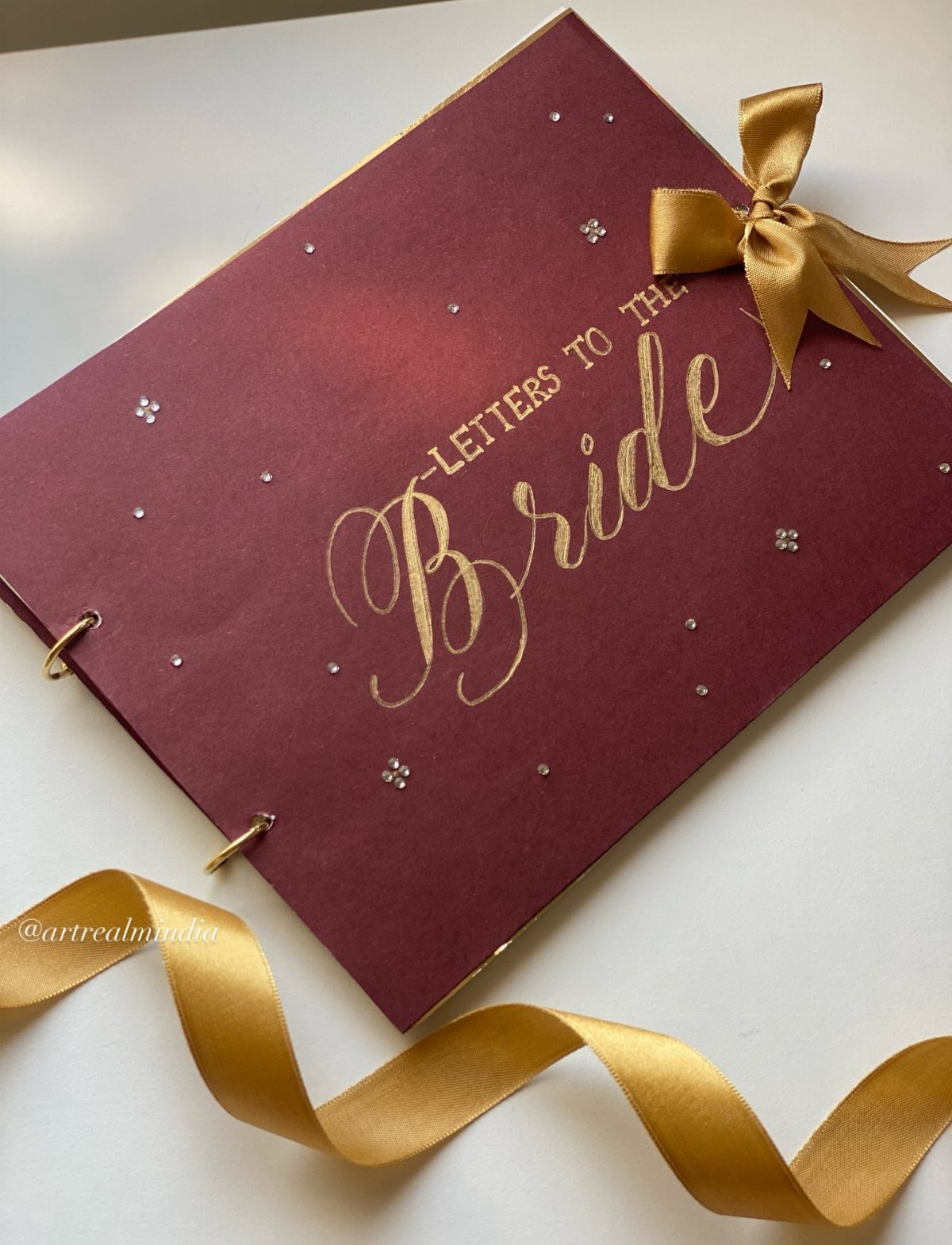 Maroon scrapbook cover with gold lettering saying Letters to the Bride and gold ribbon.