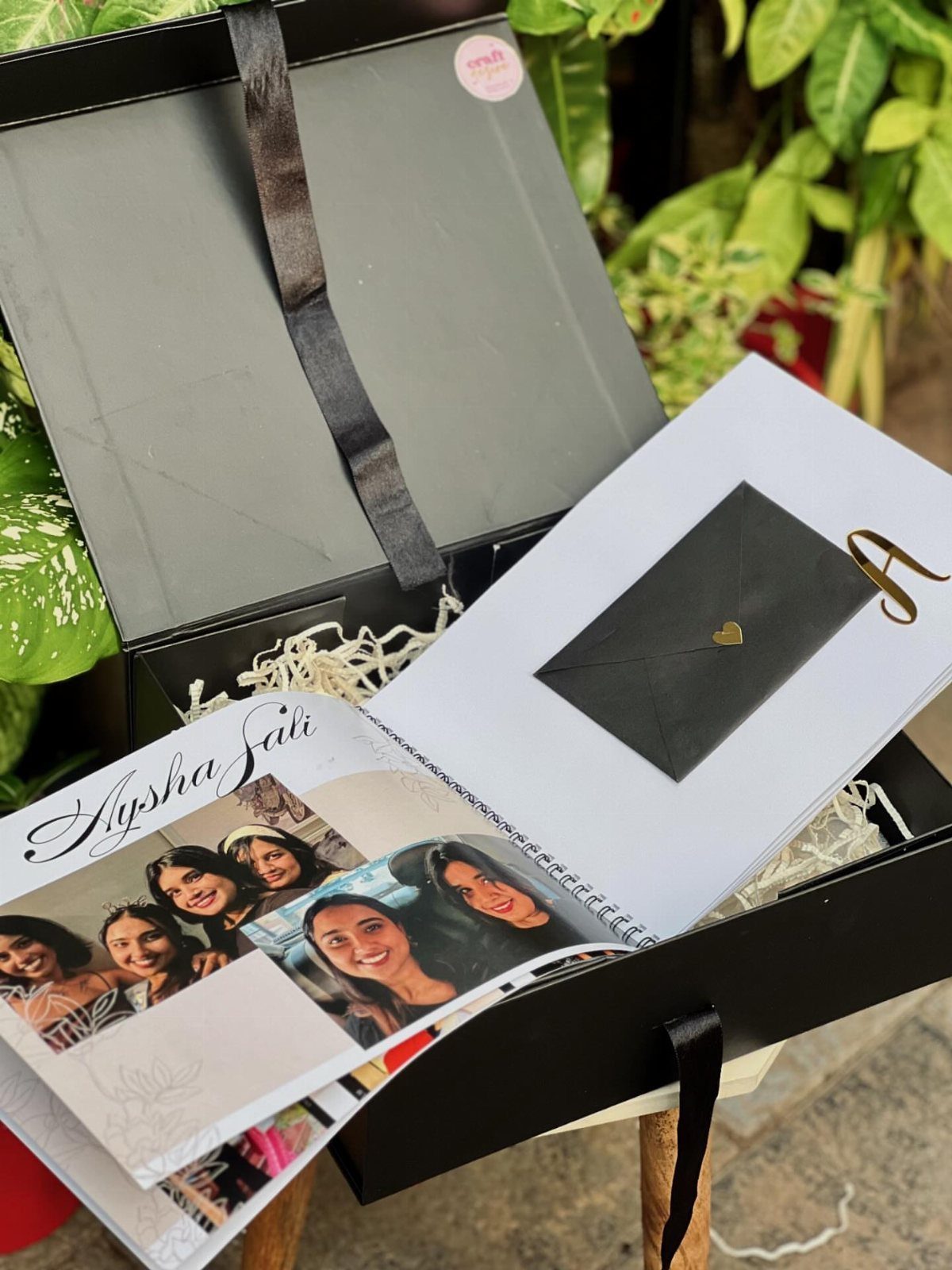 Open spiral scrapbook with photo collages and a black envelope in a gift box