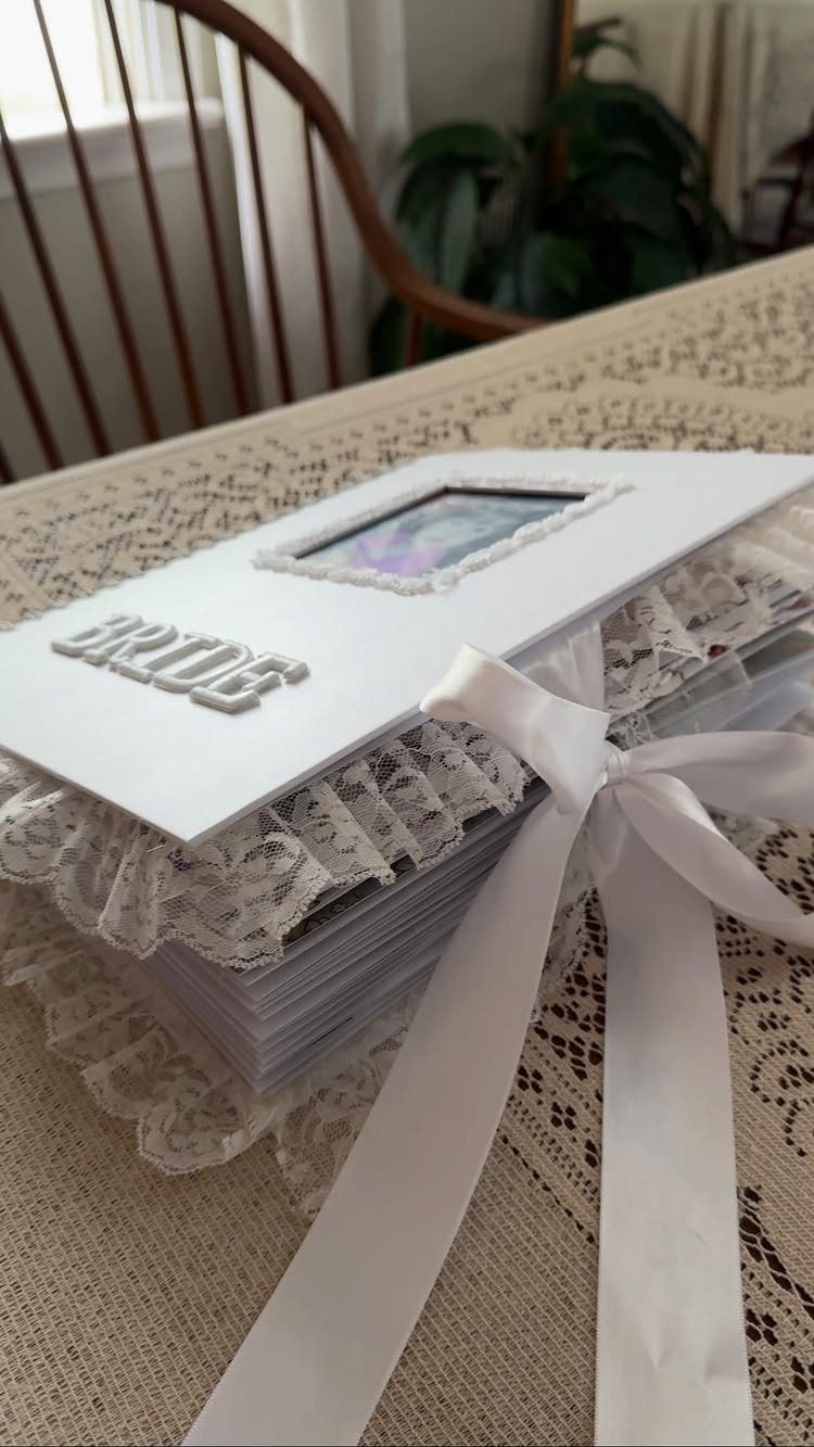 White bride scrapbook with lace trim, a ribbon bow, and a small photo.