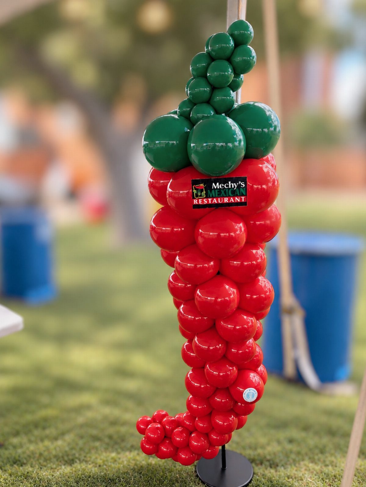 Large red chili pepper balloon sculpture with green stem on a grassy field