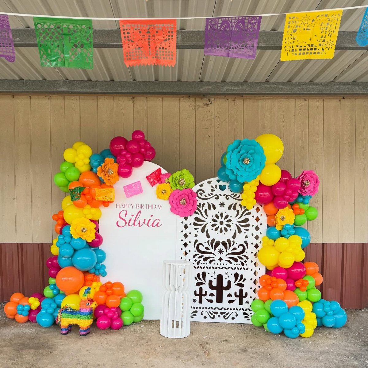 Colorful balloon arches and paper flowers surrounding a white decorative Mexican door backdrop.