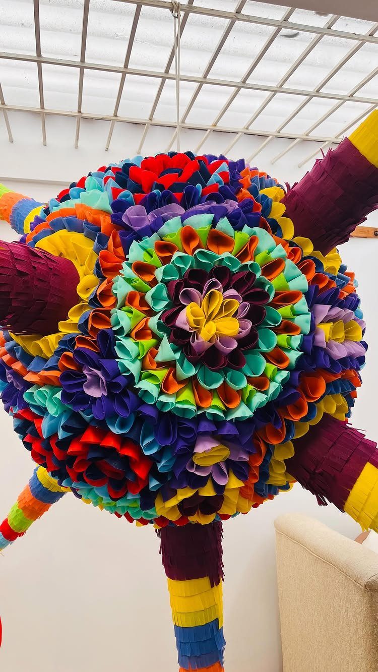 Colorful star-shaped piñata with vibrant fringed tissue paper hanging from a ceiling grid.