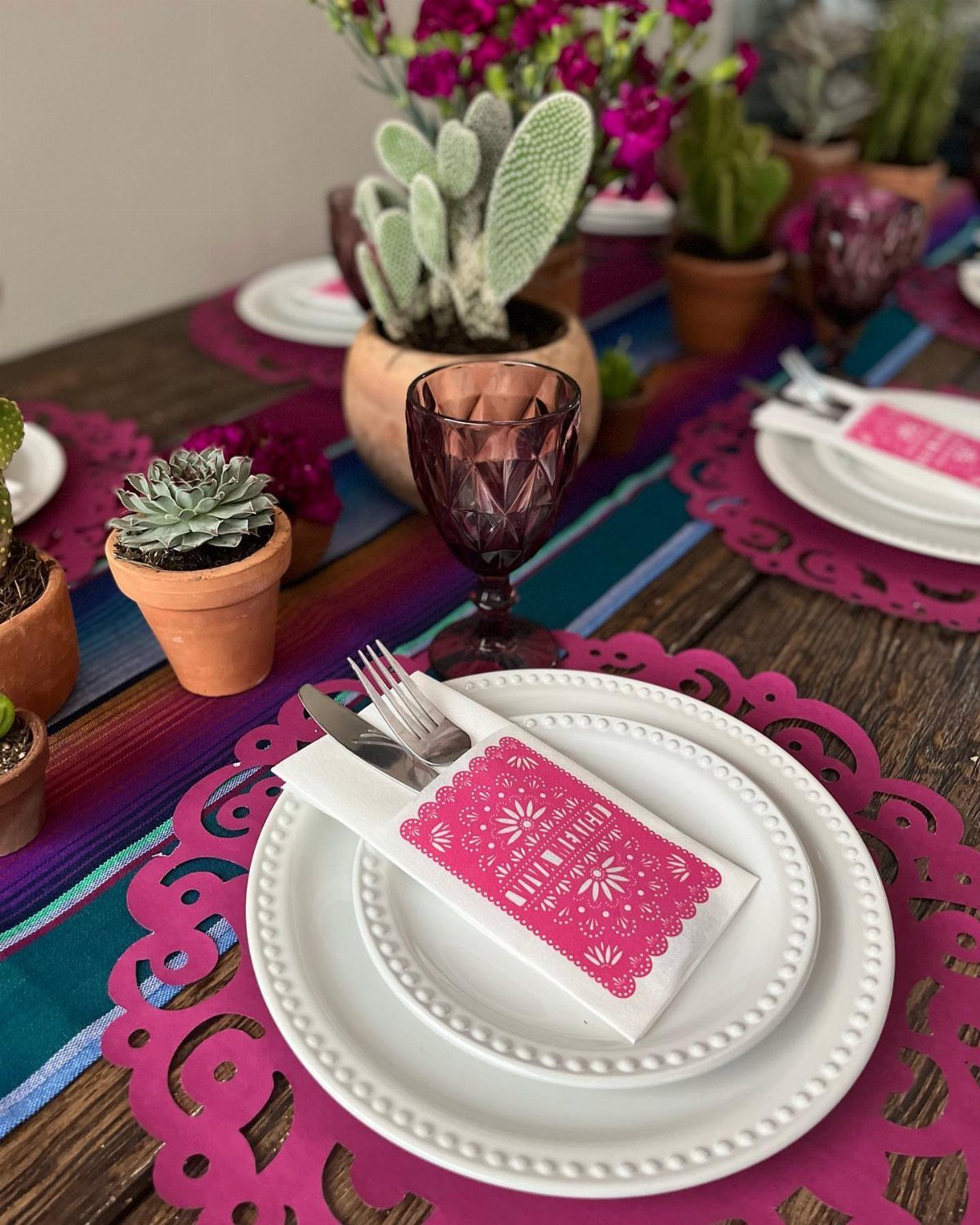 Mexican themed table setting with colorful runners, pink placemats, and small potted cacti.