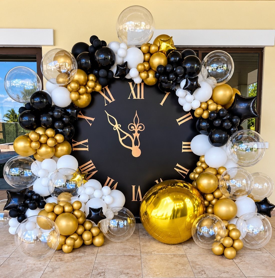 Large black clock face surrounded by gold, black, and white balloon arch decoration.