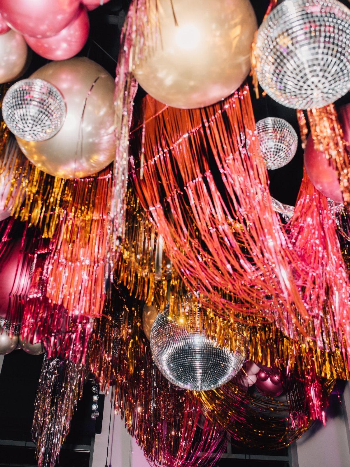 Disco balls and balloons hanging among shimmering metallic foil fringe curtains.