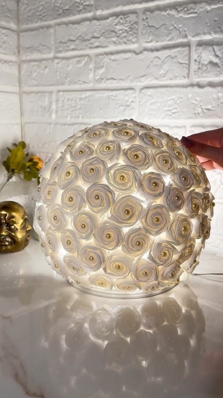 Spherical rose-patterned lamp glowing white and gold on a reflective white surface