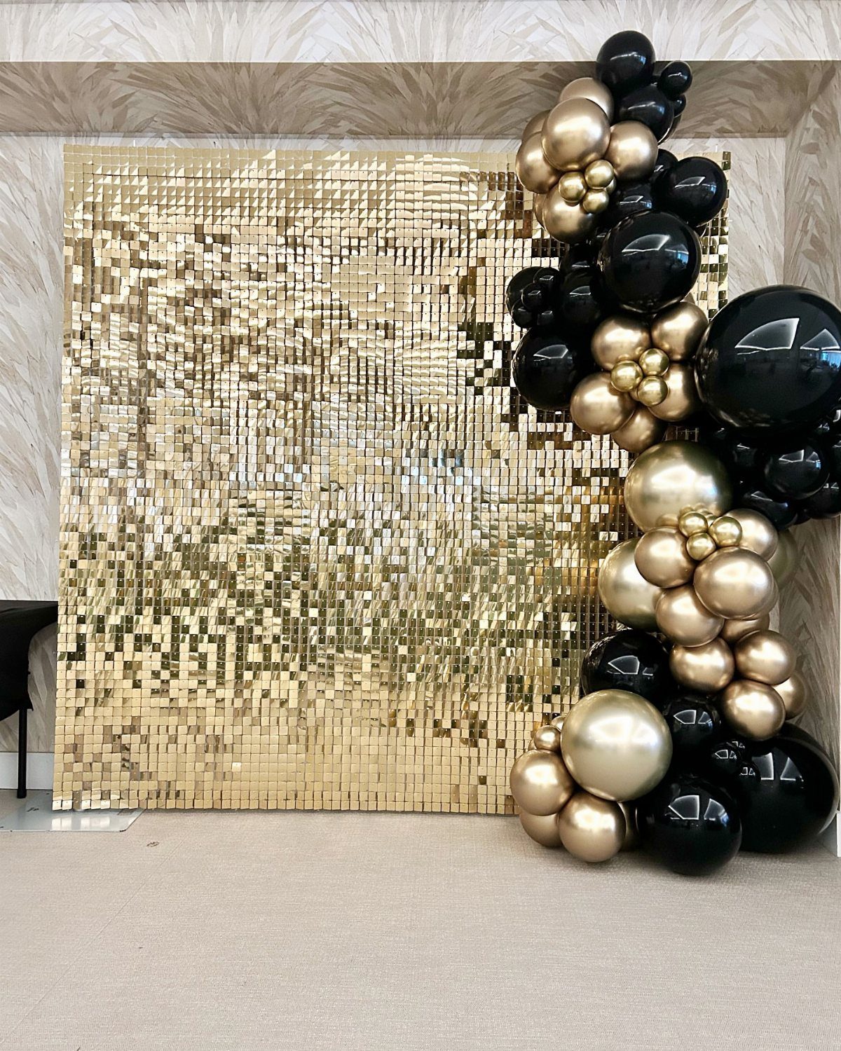Gold sequin wall backdrop with a black and gold balloon arch decoration.