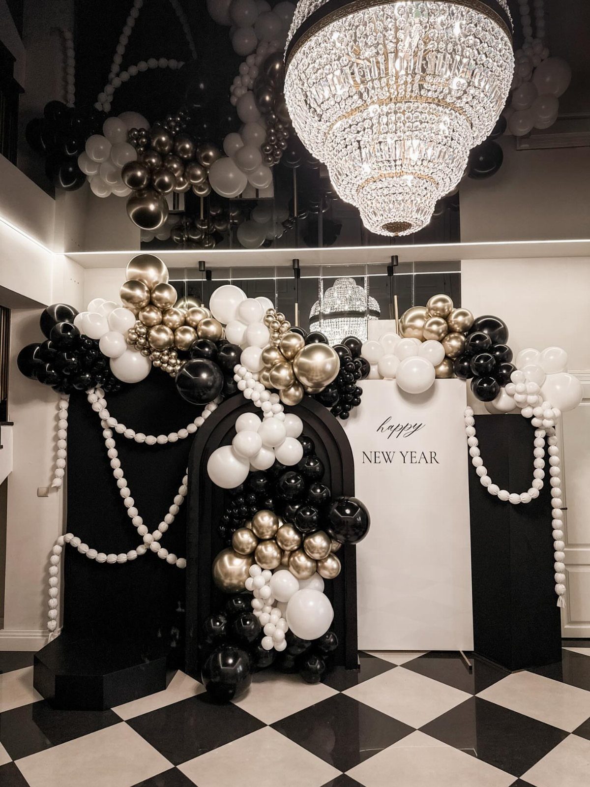 New Year's party decor with black, white, and gold balloons on checkered flooring.