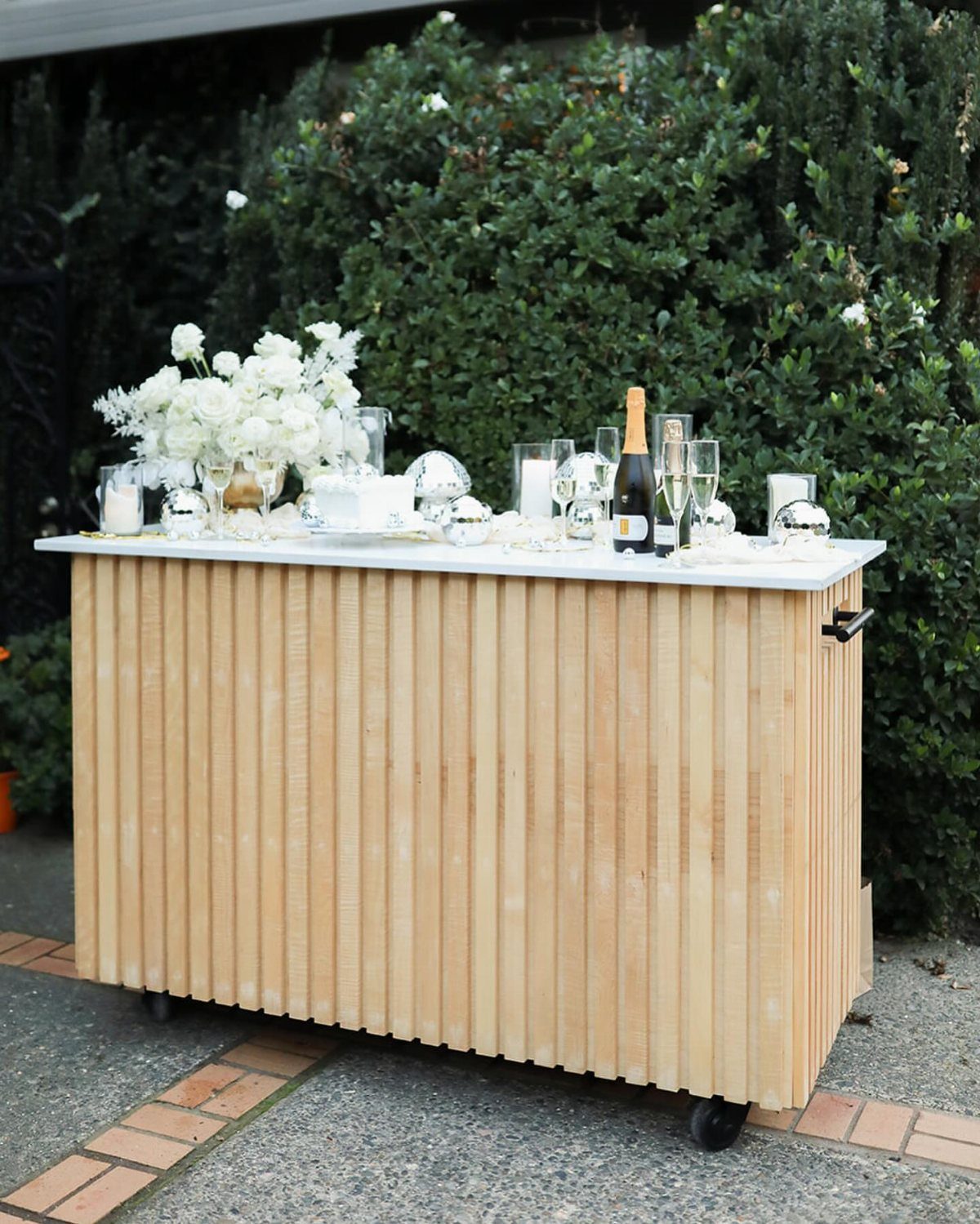 Wooden bar counter with white cake, champagne, and white flowers outdoors