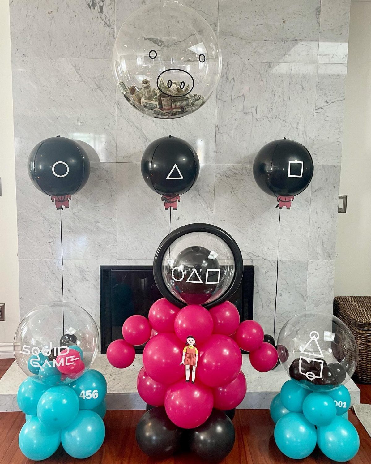 Squid Game themed party decorations with black, pink, and teal balloons and symbols.