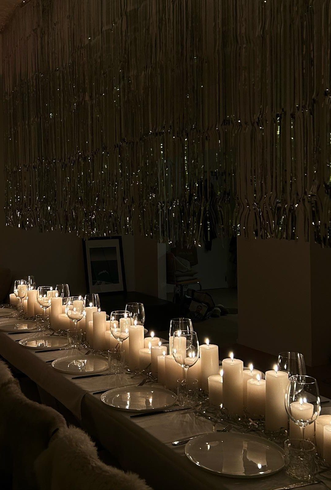 Dining table with white plates and glowing candles under silver tinsel curtains