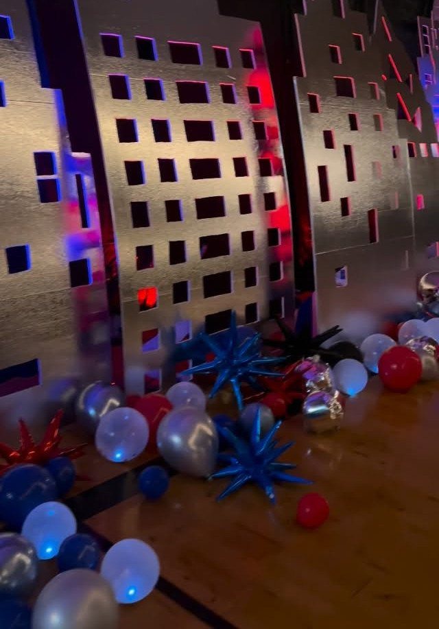 Silver skyscraper cutouts with red, white, and blue balloons on a wooden floor.