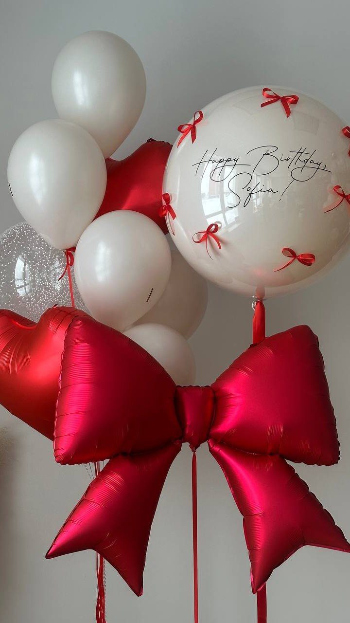 Balloon bouquet with white balloons, a personalized clear balloon, and a red foil bow.