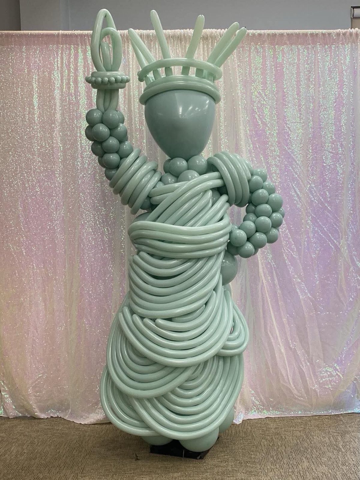 Statue of Liberty balloon sculpture standing before a sparkling pink and white backdrop