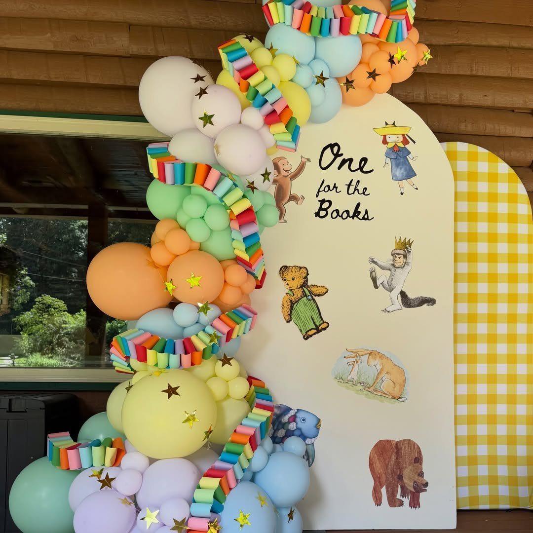 Birthday backdrop with 'One for the Books' text, book characters, and colorful balloons.