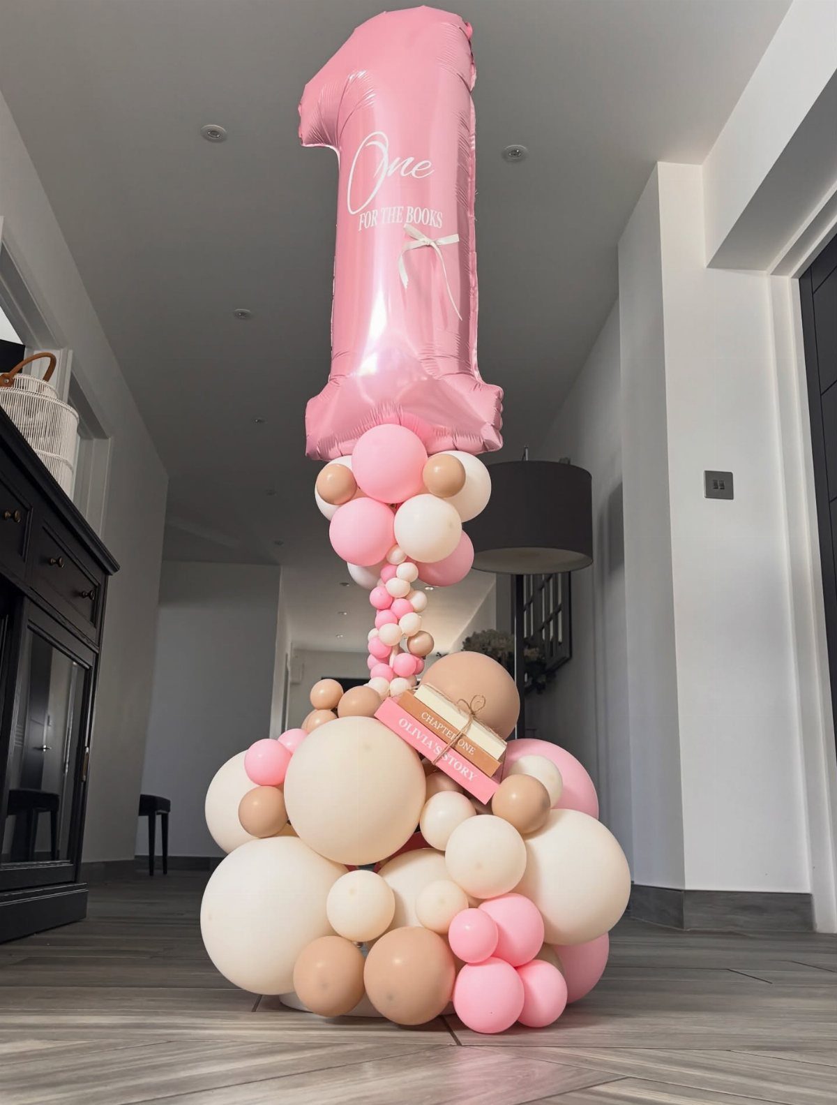 Pink number one balloon on a cluster of pink and beige balloons with a book.
