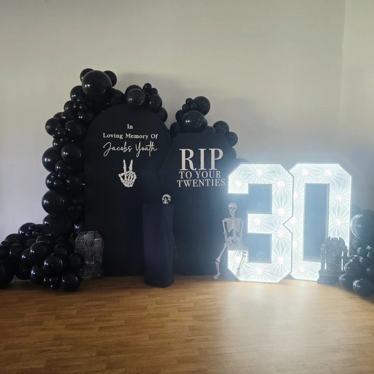 Black balloons and tombstone signs with illuminated number 30 for a birthday party.