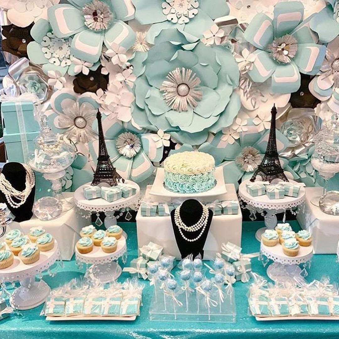 Dessert table with light blue paper flowers, Eiffel Tower miniatures, and pearl necklaces.