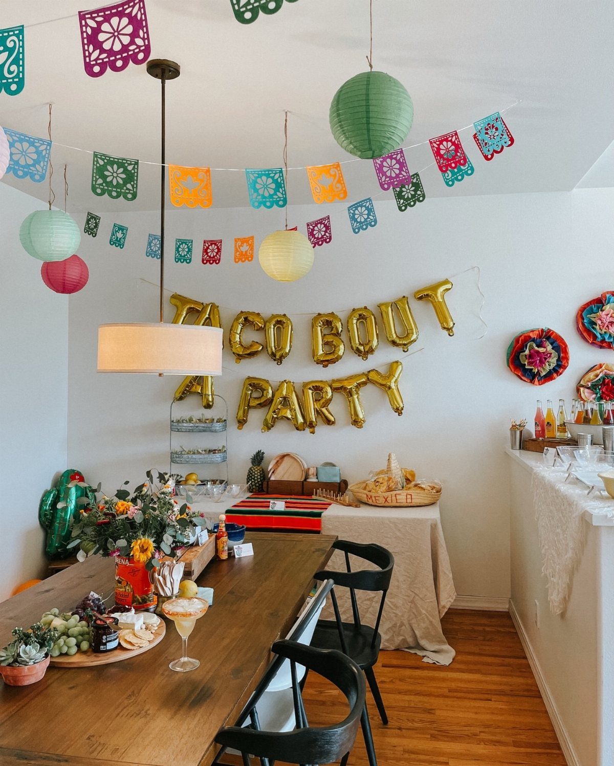 Festive party decorations with colorful banners and gold taco themed balloons over food.