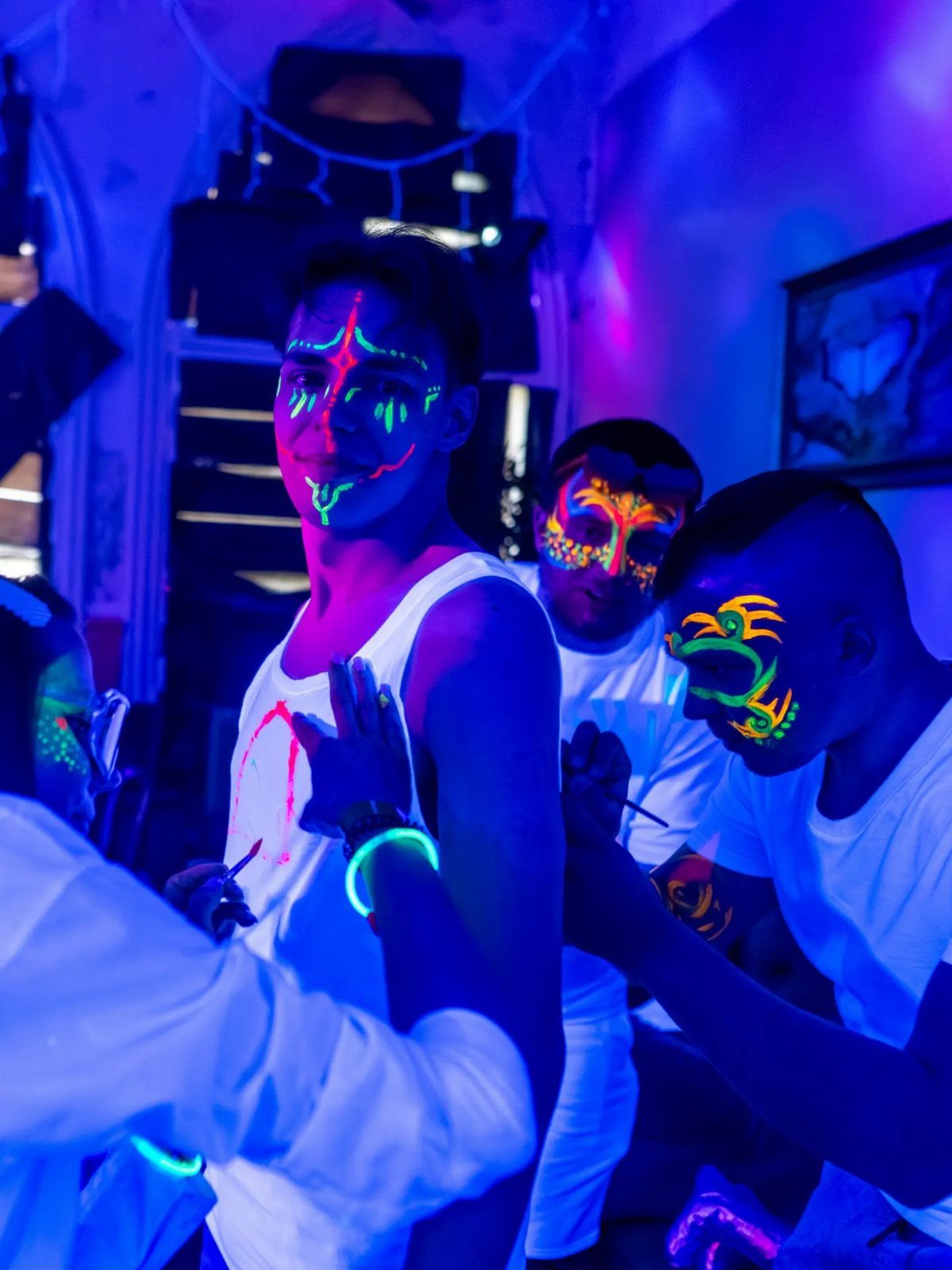 Young men with neon glow-in-the-dark face paint under blue and purple UV lights.