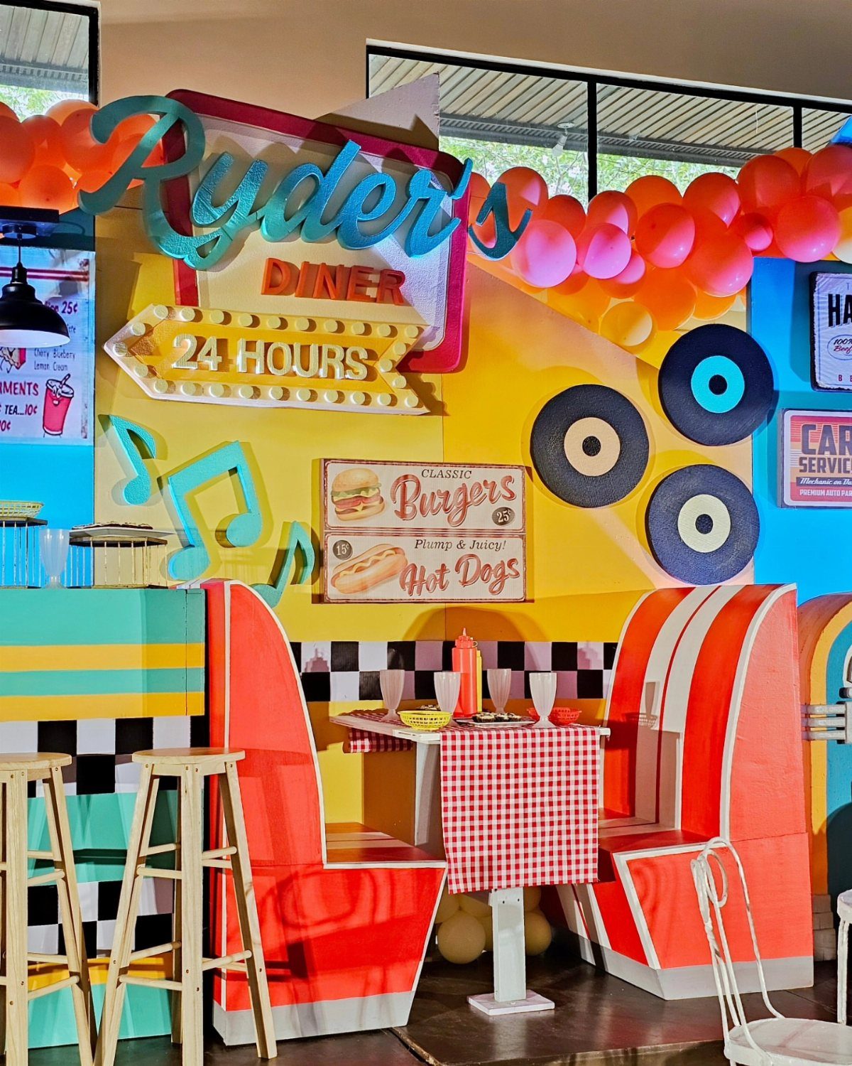 Retro diner party setup with red booths, checkered tablecloth, and vinyl record decorations.