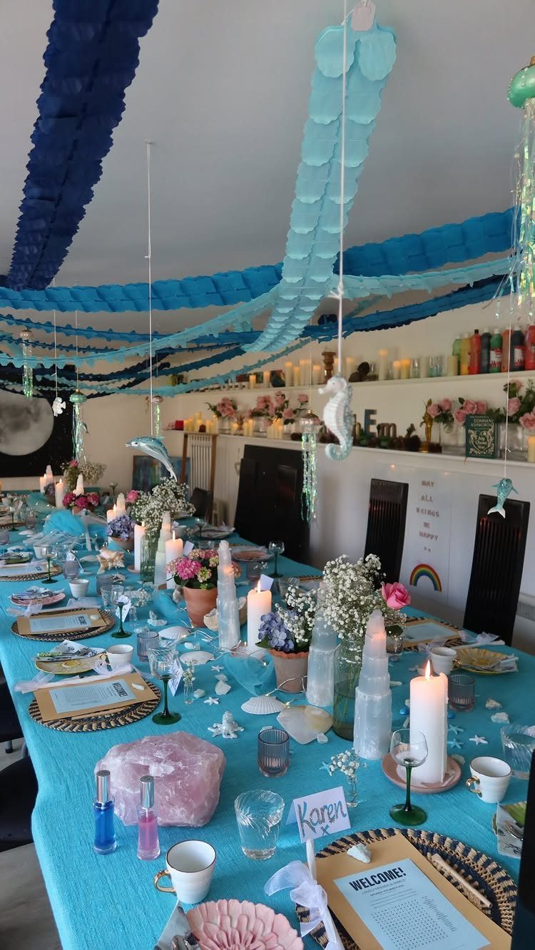 Blue table setting with seashells and turquoise paper garlands hanging from the ceiling.