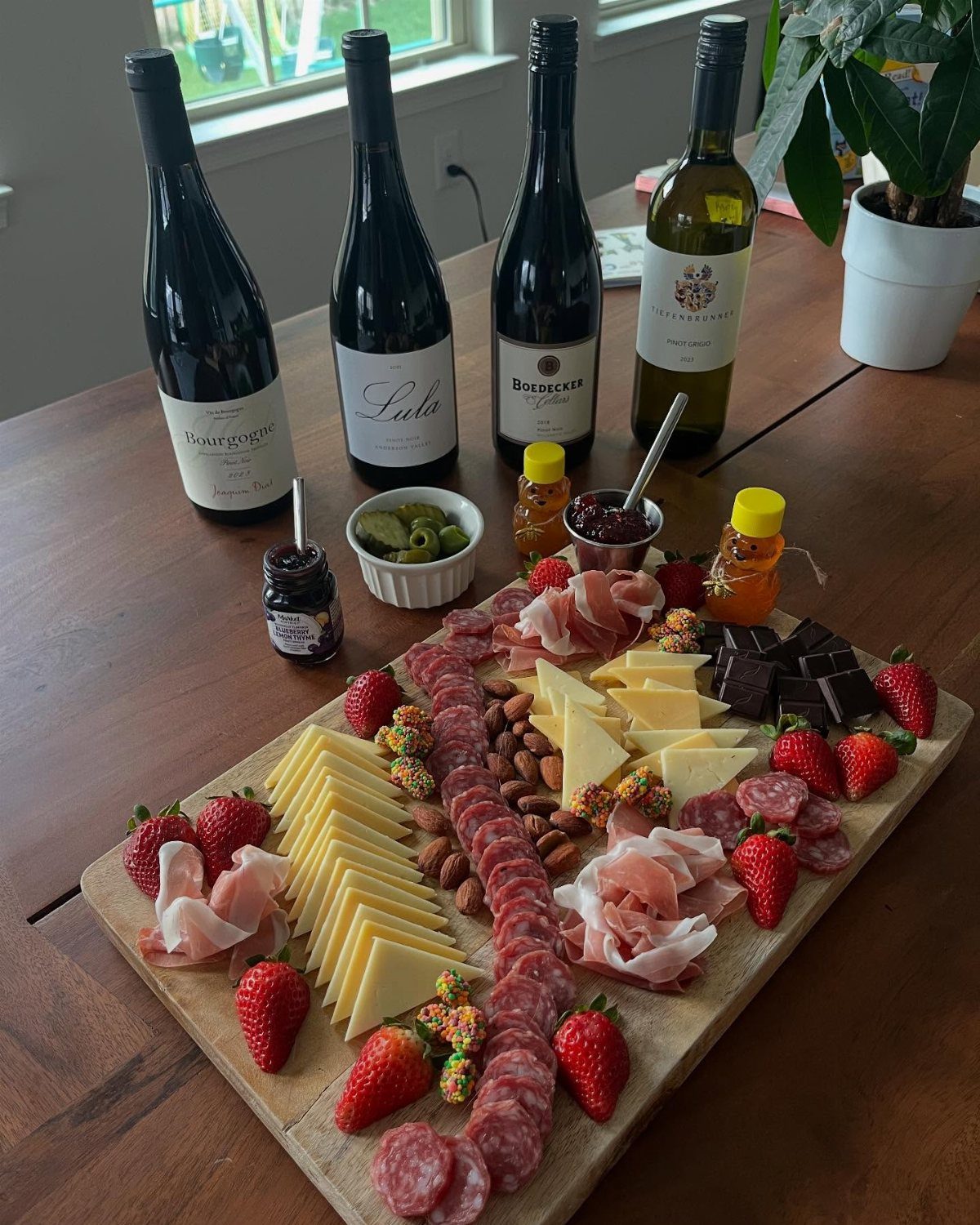 Wine bottles and a wooden charcuterie board with cheese, meats, and strawberries.