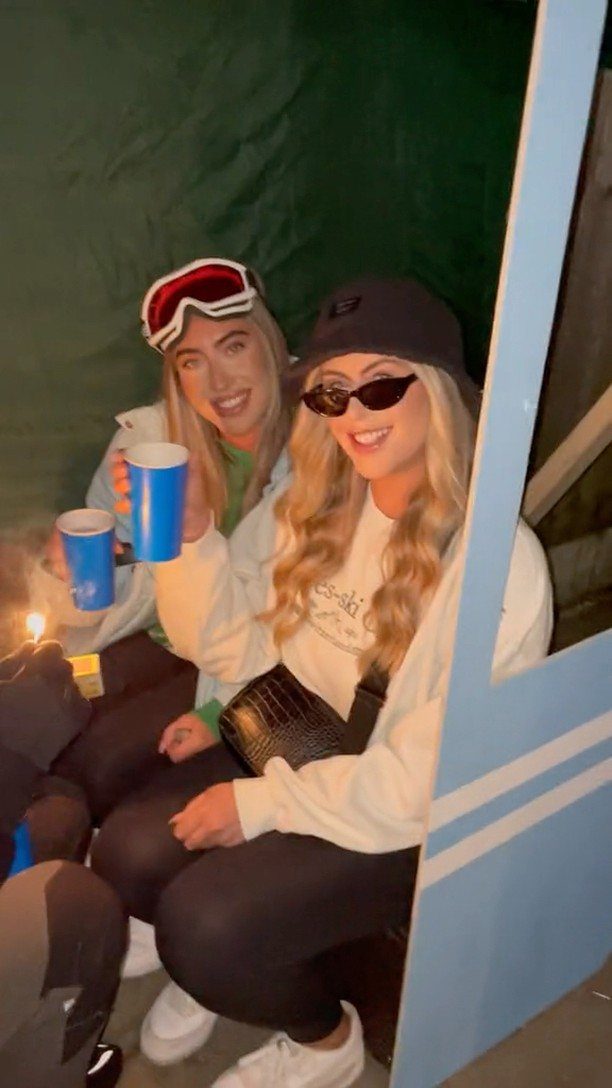 Two women in ski attire holding blue cups at a winter themed party.