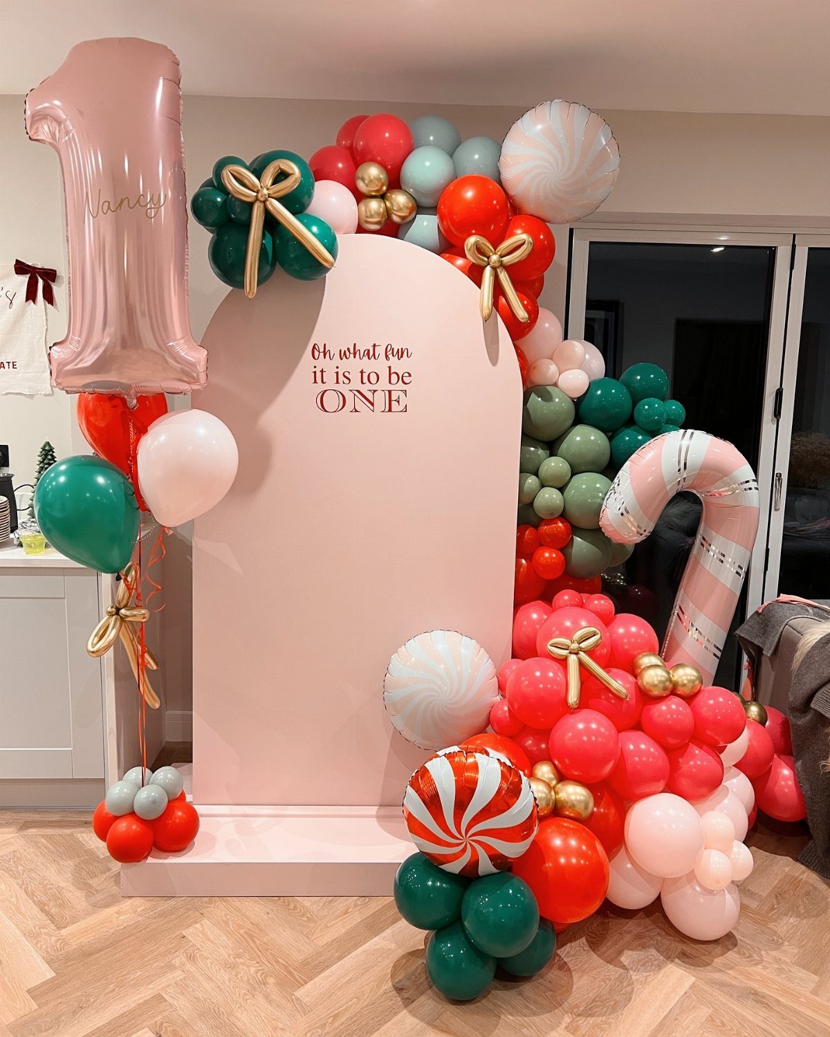 First birthday party decoration with pink backdrop, red and green balloons, and candy cane.